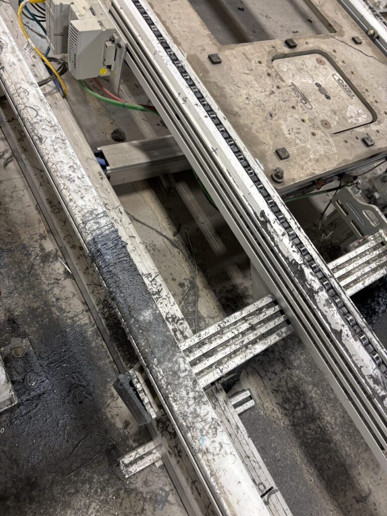 Cured adhesive strings and buildup caked on aluminum conveyor rails before dry ice cleaning